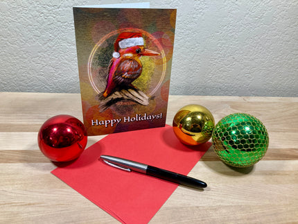 Happy Holidays card with a bird illustration, red pen, and Christmas ornaments on a wooden surface.