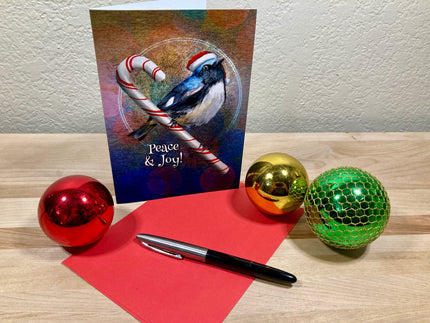 Christmas card with a bird and candy cane, surrounded by decorative balls and a pen on a wooden surface.