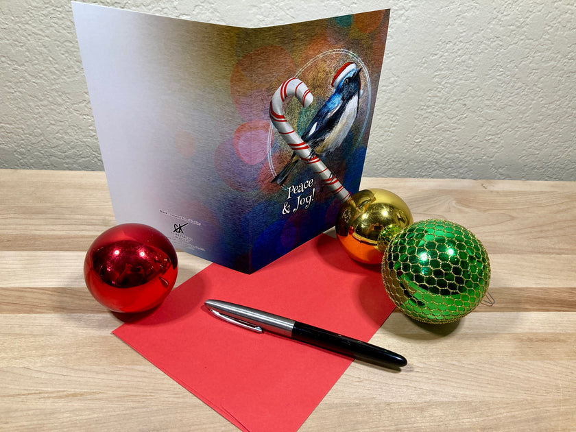 Greeting card with candy cane and bird design, surrounded by Christmas ornaments on a wooden surface.