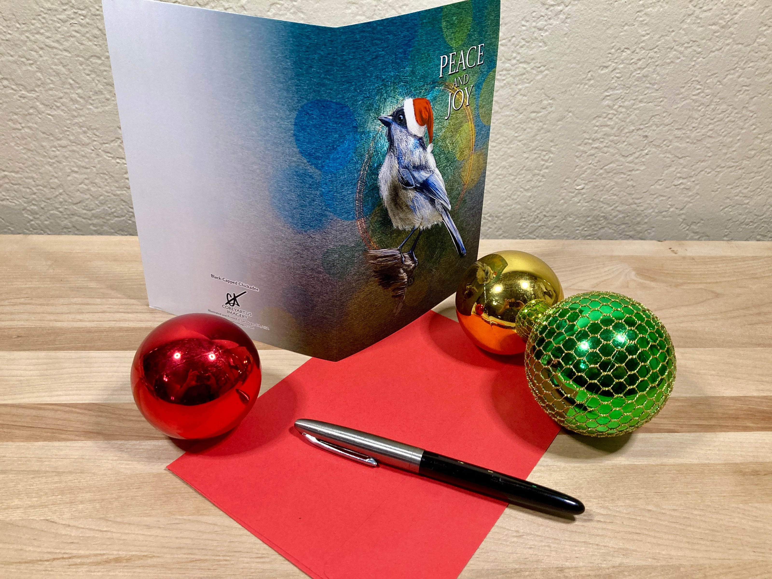 Card with a bird illustration, pen, and Christmas ornaments on a wooden surface.