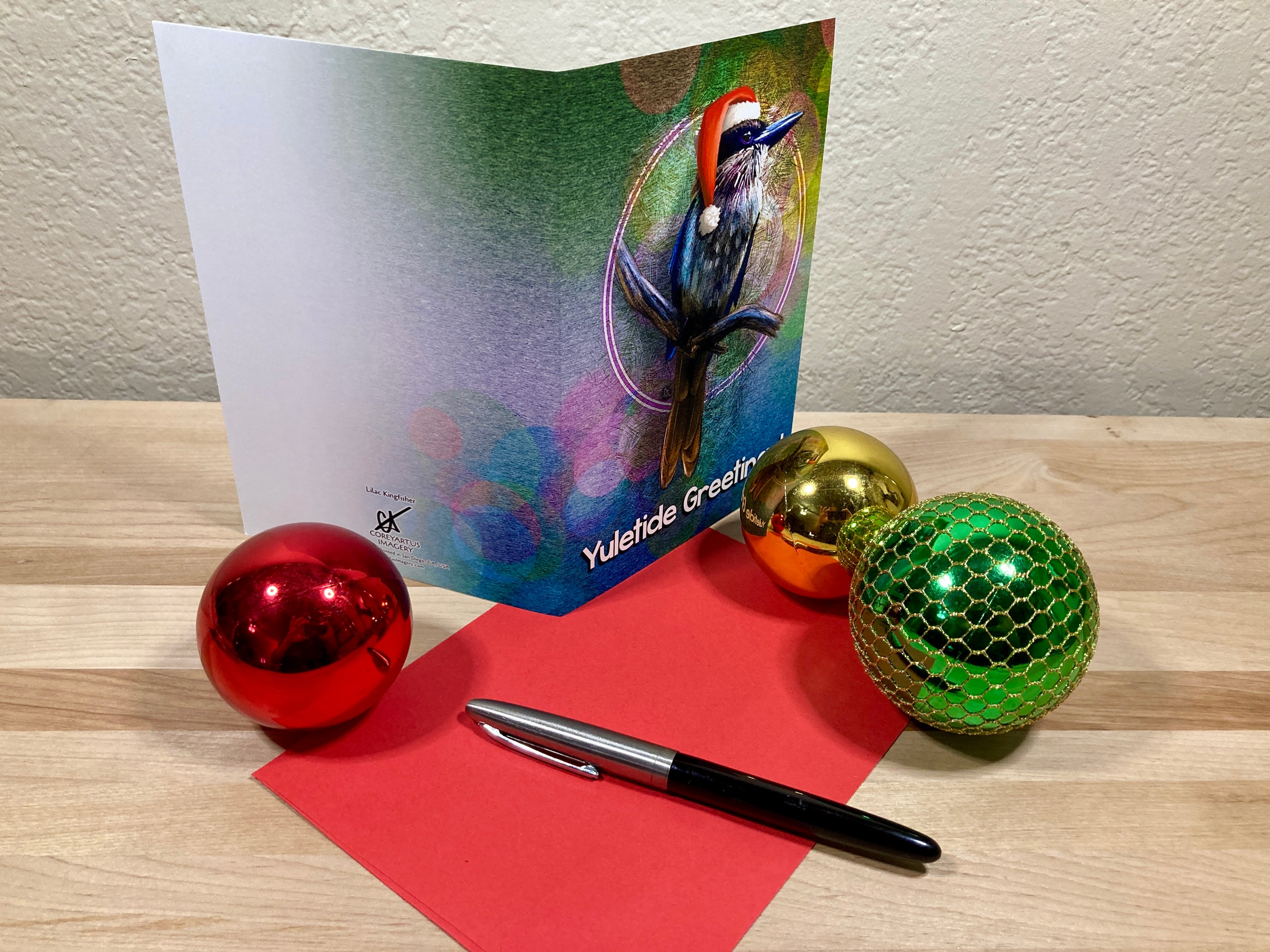Greeting card with colorful design, pen, and decorative balls on a wooden surface.