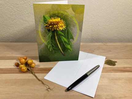 Greeting card with dandelion design, envelope, pen, and decorative elements on a wooden surface.