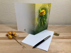 Greeting card with floral design, envelope, and pen on a wooden surface.
