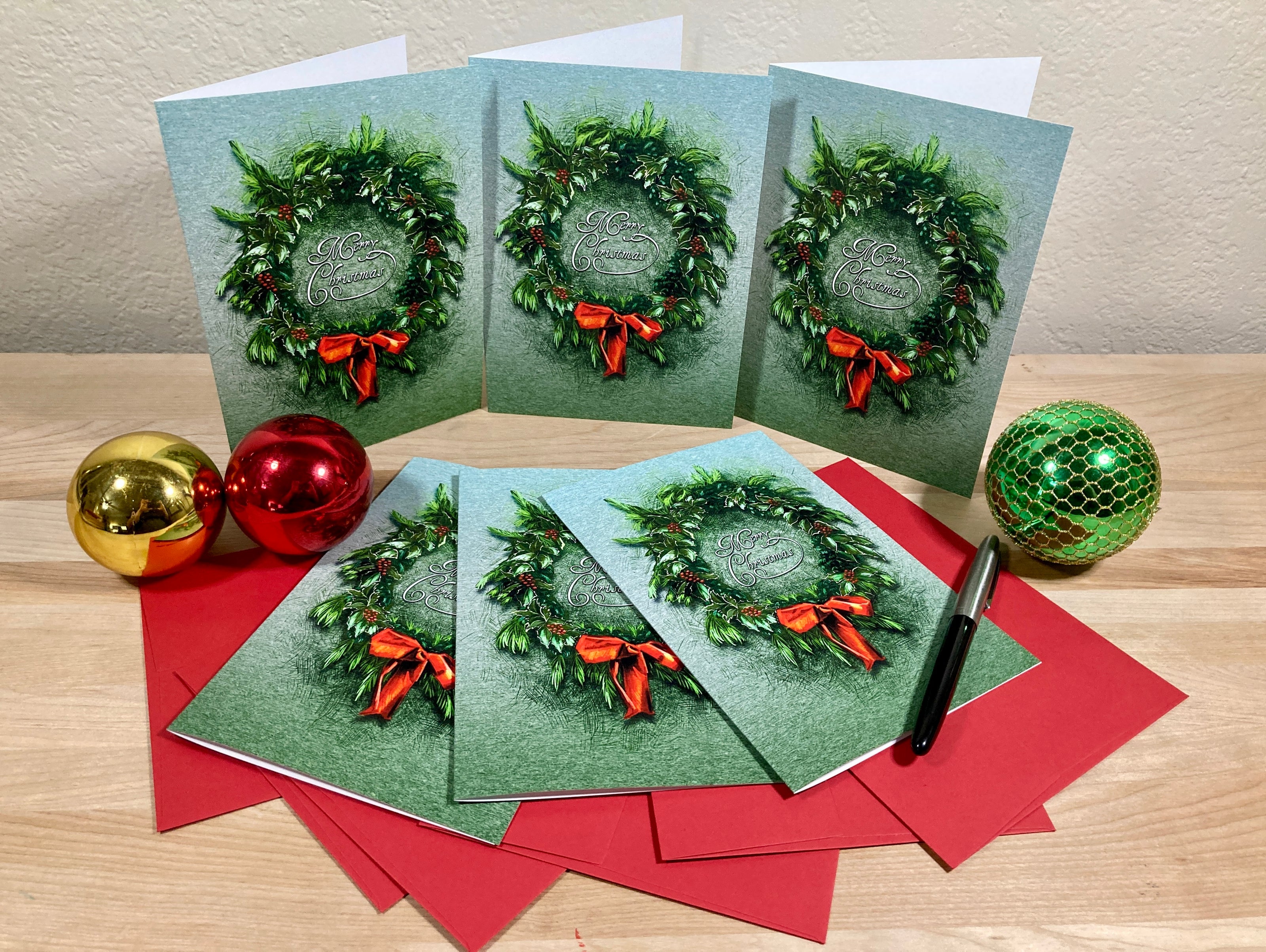 Set of Christmas cards with wreath designs on a wooden surface with decorative balls.