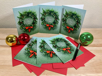 Set of Christmas cards with wreath designs on a wooden surface with decorative balls.