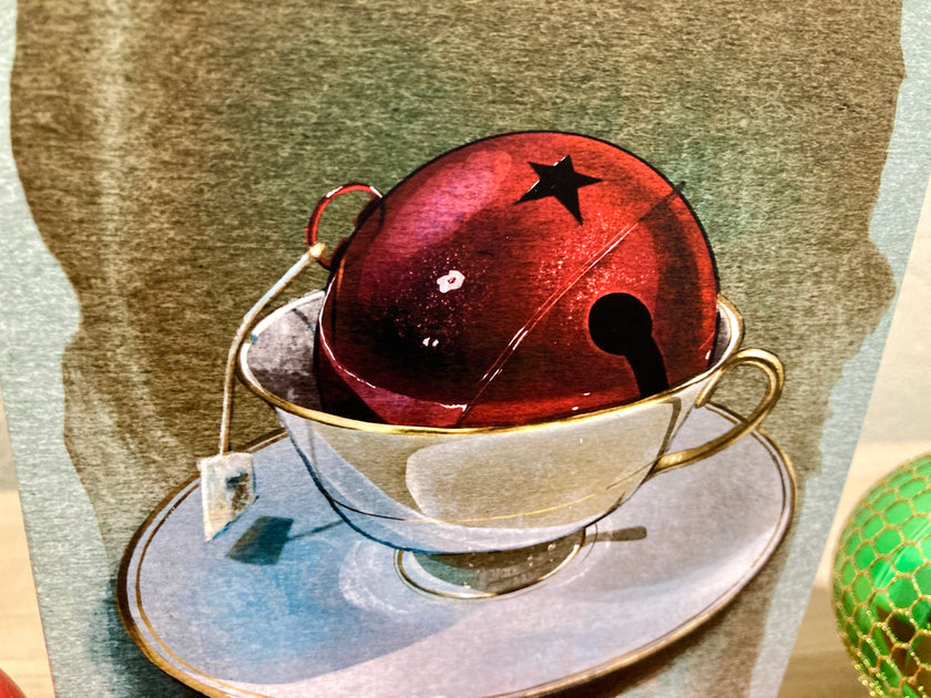 Red bell with a star on top inside a teacup on a saucer with a green decorative element.