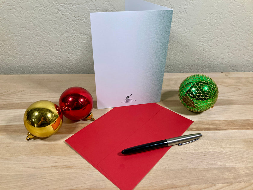 Greeting card, red envelope, pen, and Christmas ornaments on a wooden surface.