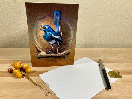 Greeting card with a blue bird illustration on a wooden surface with an envelope and pen.