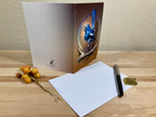 Greeting card with a bird design on a wooden surface with a pen and small decorative items.