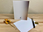 Greeting card, envelope, pen, and decorative berries on a wooden surface with a textured wall background.