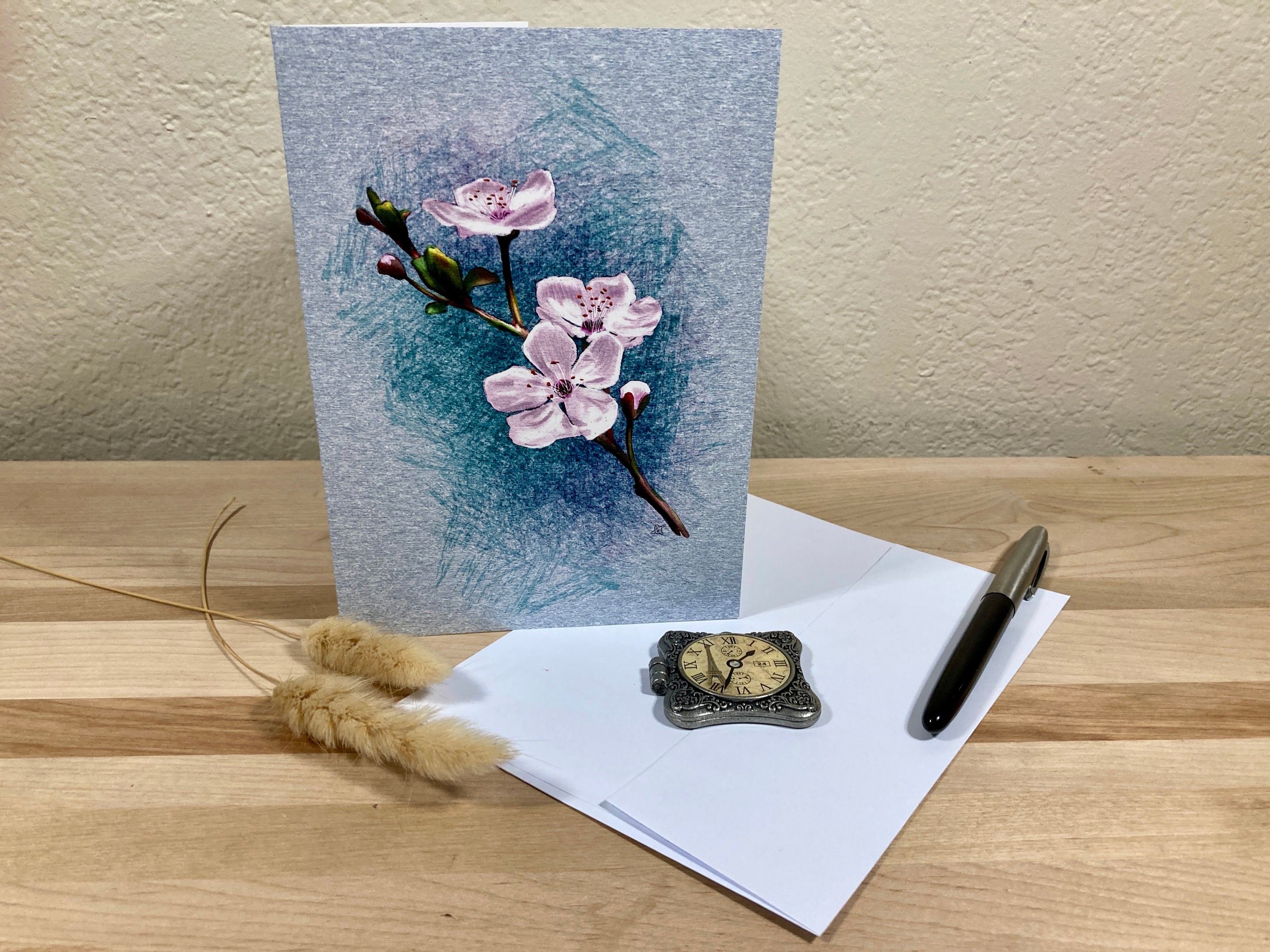 Greeting card with floral design on a wooden surface with an envelope and decorative items.
