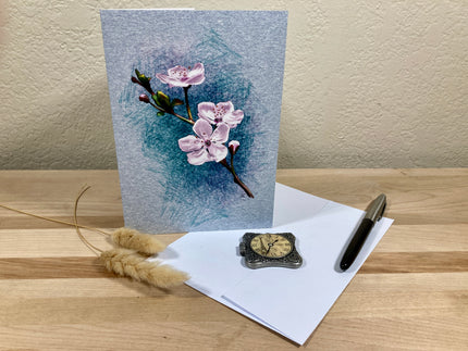 Greeting card with floral design on a wooden surface with an envelope and decorative items.
