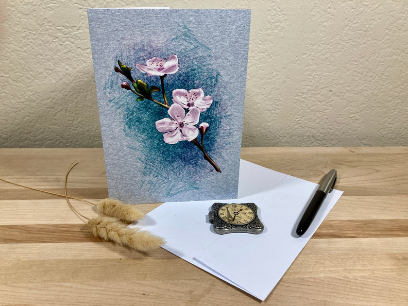 Greeting card with floral design on a wooden surface with an envelope and decorative items.
