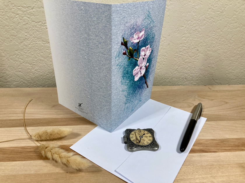Floral card on a wooden surface with a pen and decorative clock.