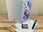 Greeting card with floral design on a wooden surface with a pen and decorative item.