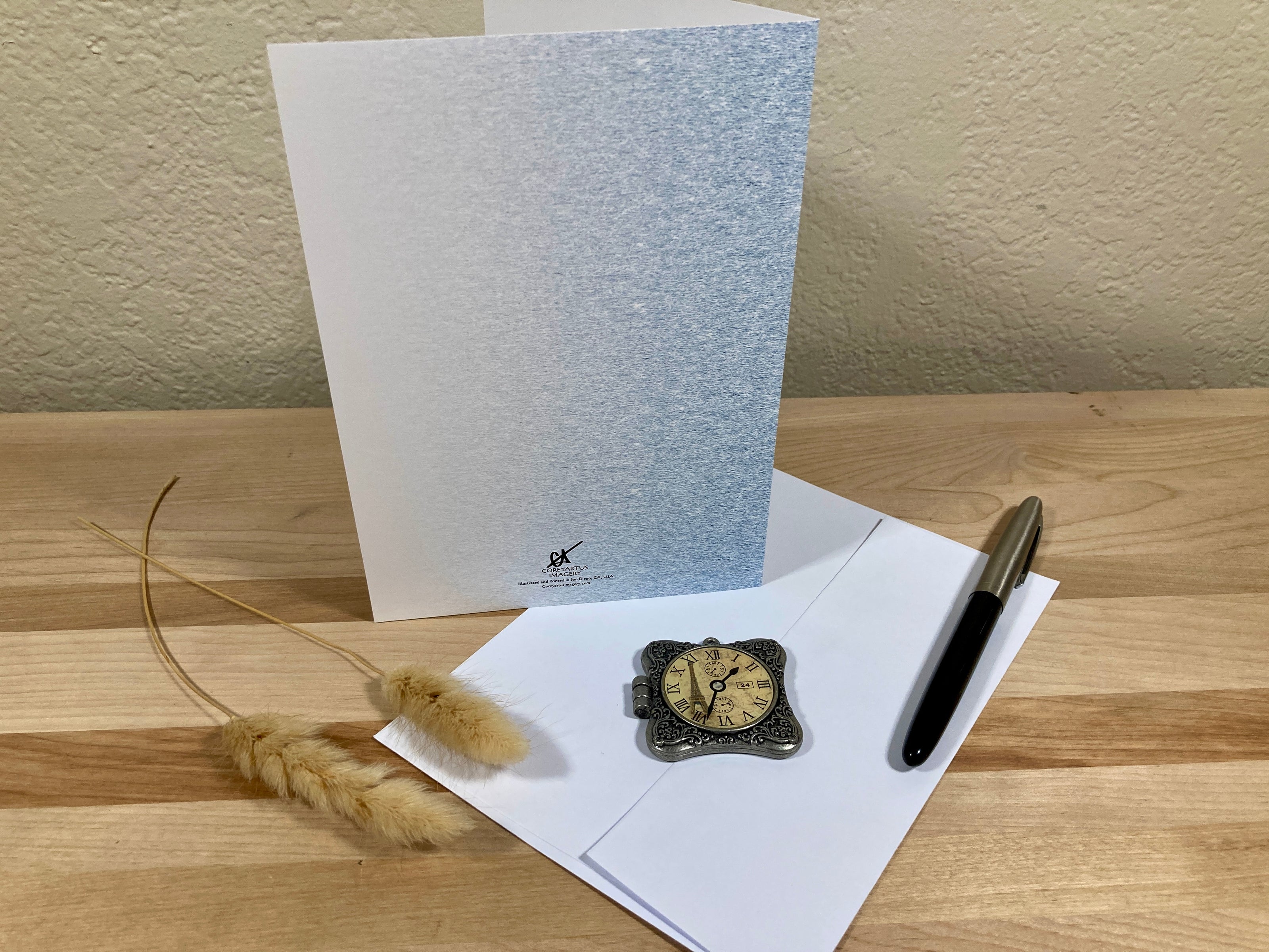 Greeting card with envelope, pen, and decorative item on a wooden surface