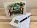 Greeting card with colorful stones on a wooden bench, envelope, and pen on a wooden surface.