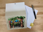 Greeting card with colorful stones on a wooden bench, envelope, and pen on a wooden surface