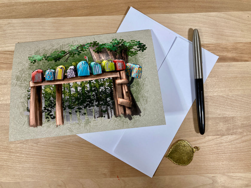 Greeting card with colorful birdhouses on a wooden bench, envelope, pen, and gold seal on a wooden surface.