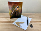 Greeting card with bird illustration on a wooden surface with a pen and feather.
