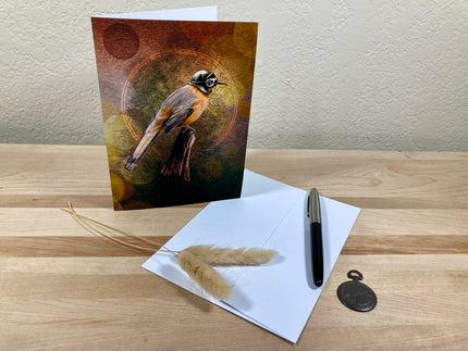 Greeting card with bird illustration on a wooden surface with a pen and feather.