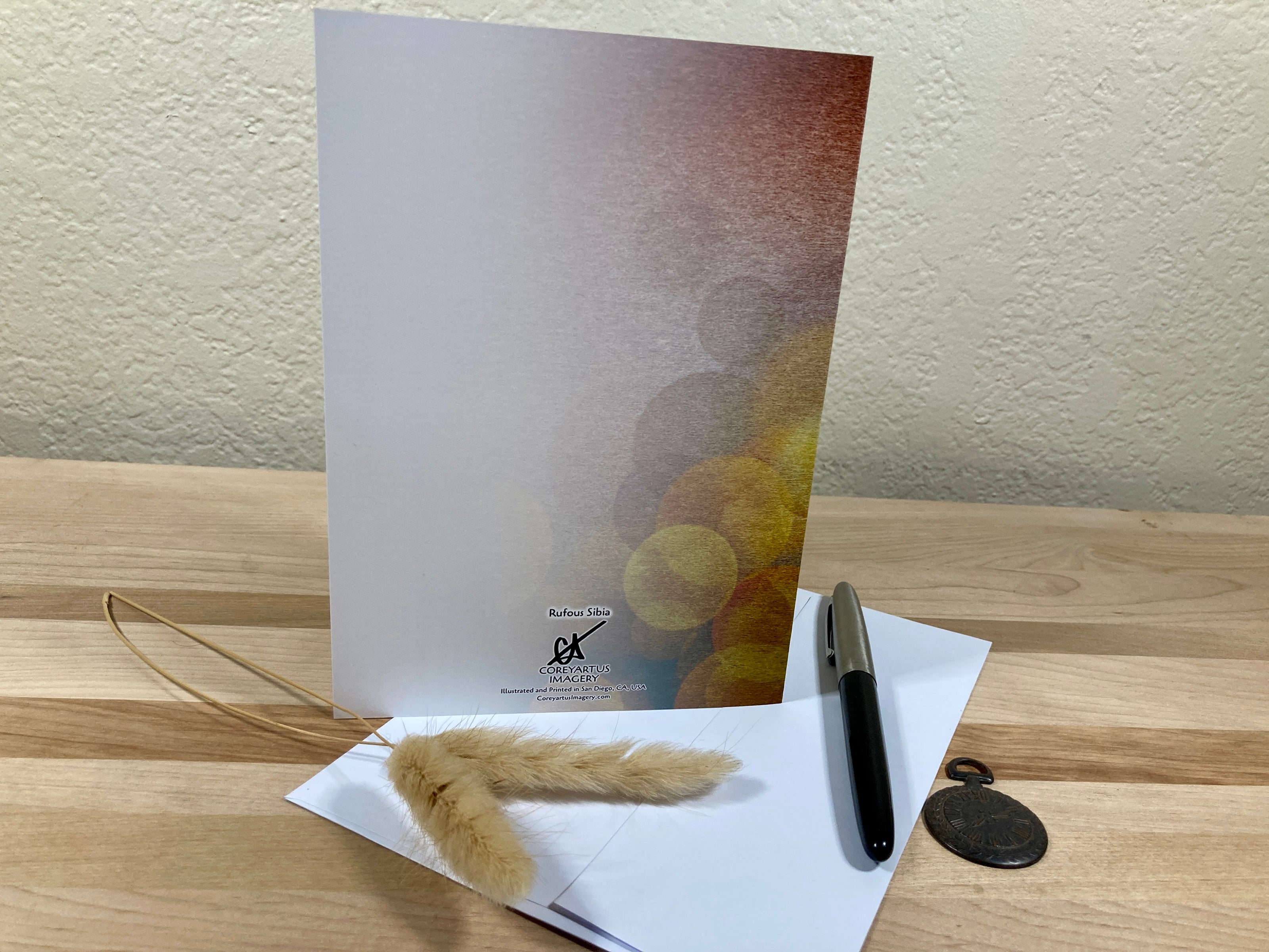 Greeting card with envelope, pen, and decorative feather on a wooden surface
