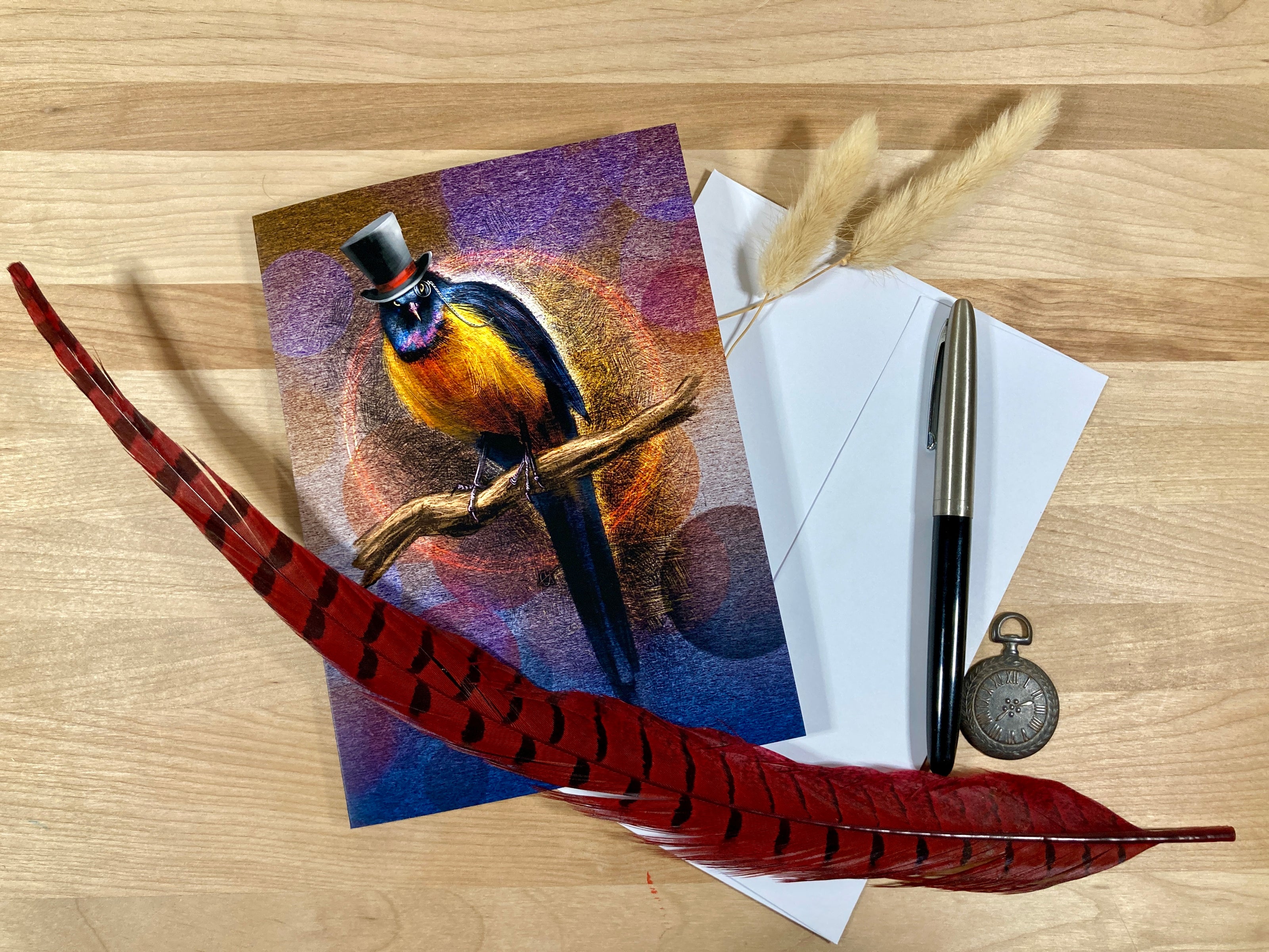 Greeting card with a bird design, envelope, pen, and feather on a wooden surface