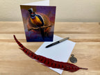 Greeting card with a bird design, feather, pen, and envelope on a wooden surface