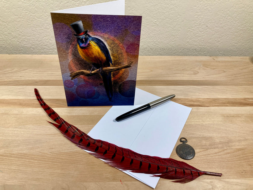 Greeting card with a bird design, feather, pen, and envelope on a wooden surface