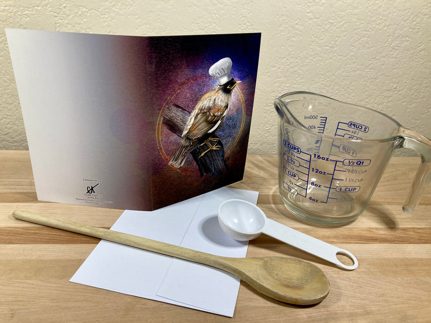Measuring cup, wooden spoon, and card with a bird design on a wooden surface