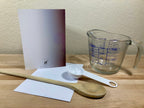 Measuring cup, wooden spoon, and white card on a wooden surface with a light background