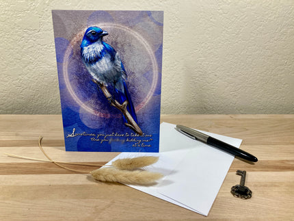Greeting card with a blue bird illustration on a wooden surface with a pen and key.