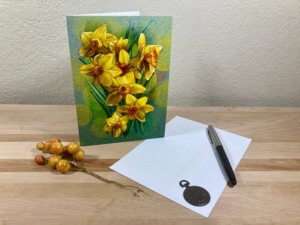 Greeting card with yellow flowers, pen, and paper on a wooden surface