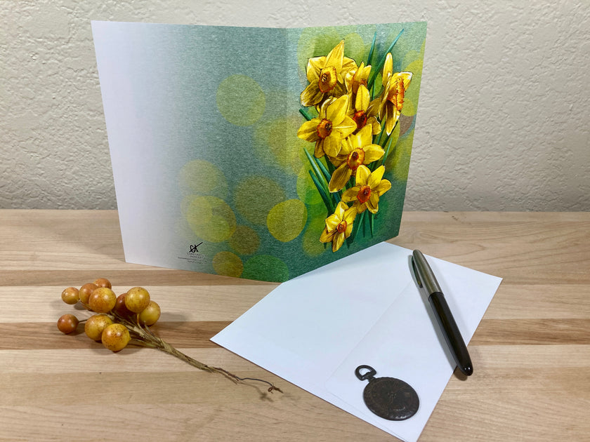 Greeting card with yellow flowers on a wooden surface with a pen and small plant.