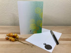 Greeting card with green abstract design, pen, and envelope on a wooden surface.