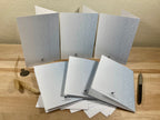Set of gray greeting cards on a wooden surface with a pen.