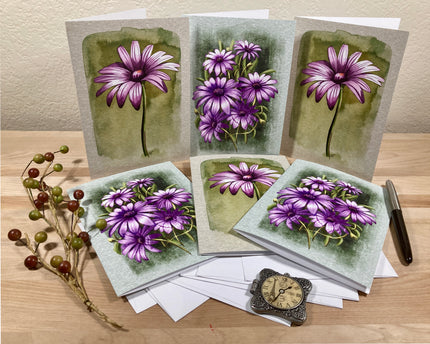 Set of greeting cards with purple flowers on a wooden surface with a pen and decorative elements.