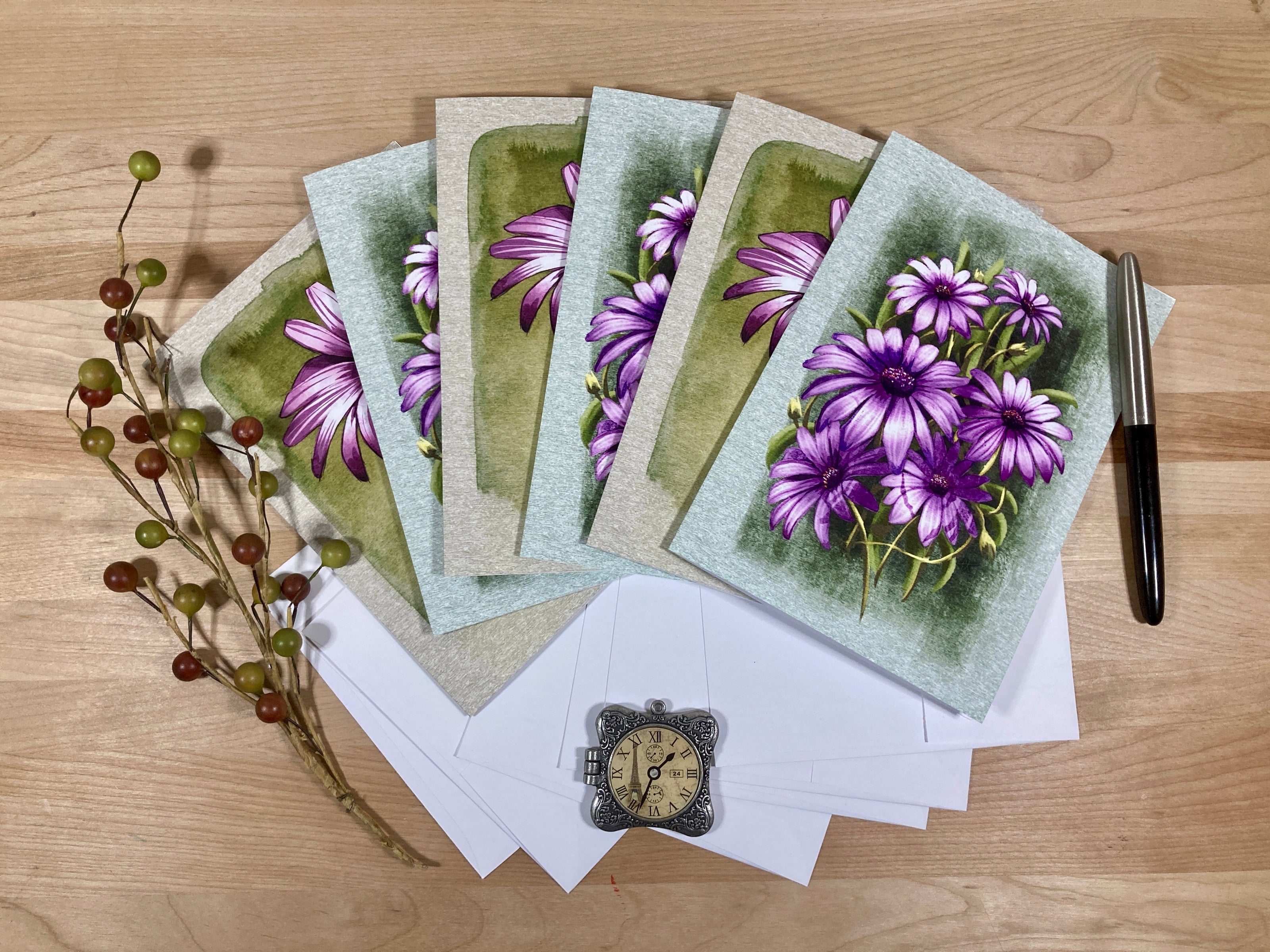 Set of greeting cards with purple flowers on a wooden surface with stationery items.