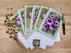 Set of greeting cards with purple flowers on a wooden surface with stationery items.