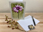 Greeting card with a purple flower illustration on a wooden surface with stationery items.