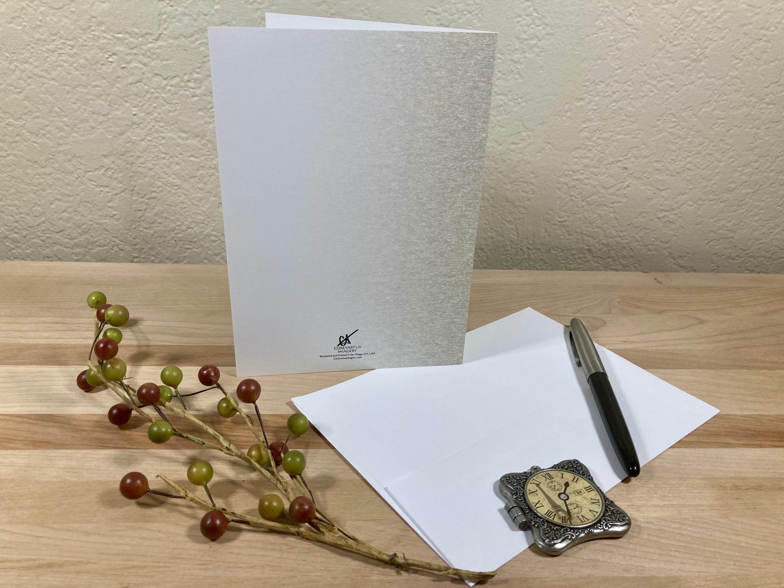 White greeting card with a pen and decorative branch on a wooden surface
