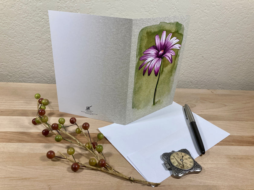 Greeting card with a flower design on a wooden surface with a pen and decorative branch.
