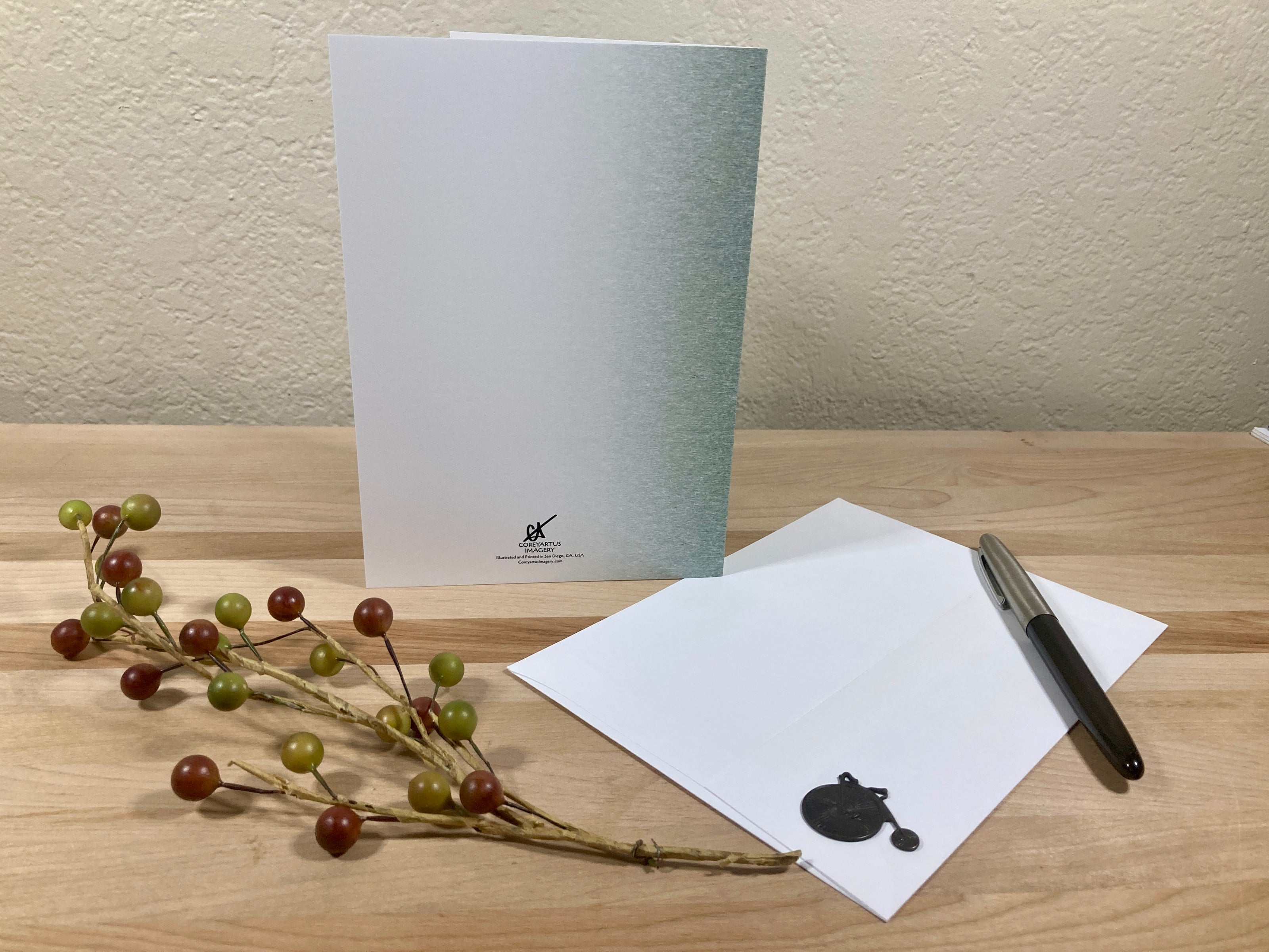 Greeting card with a pen and decorative branch on a wooden surface
