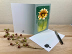 Greeting card with a sunflower design on a wooden surface with a pen and decorative branch.