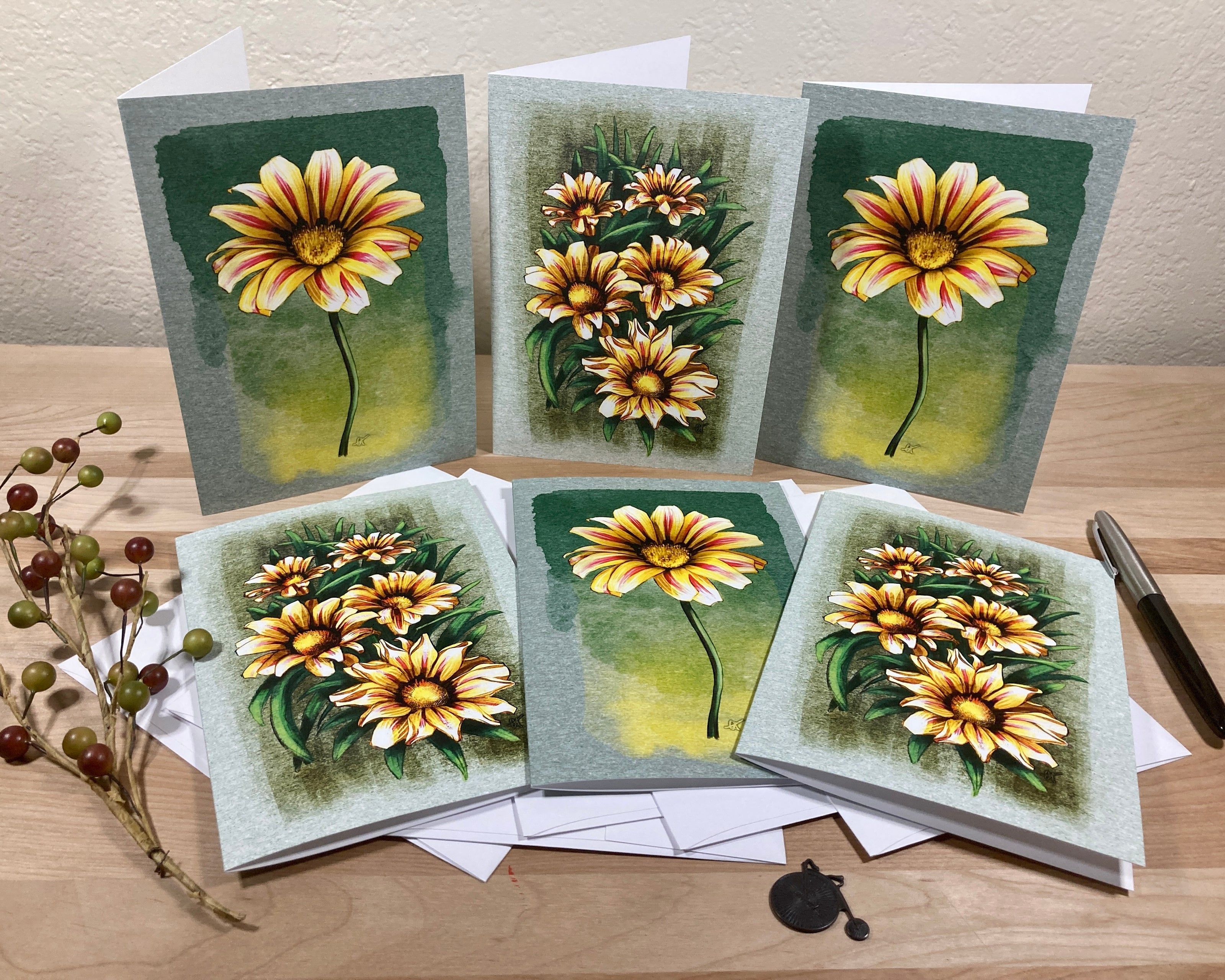Set of six floral greeting cards on a wooden surface with a pen and small plant.