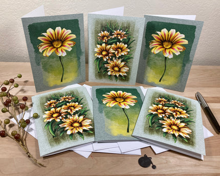 Set of six floral greeting cards on a wooden surface with a pen and small plant.