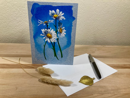 Greeting card with floral design on a wooden surface with a pen and leaves.