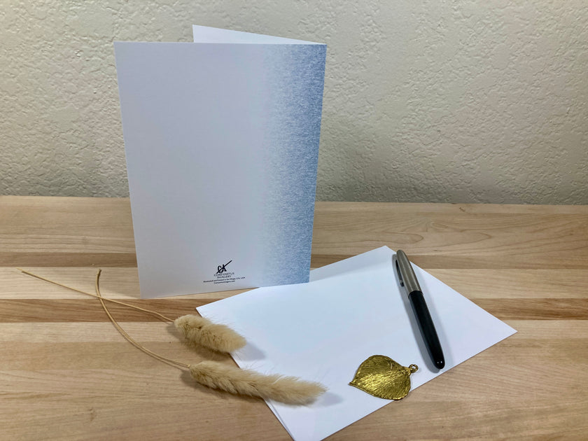 Greeting card, envelope, pen, and decorative elements on a wooden surface.