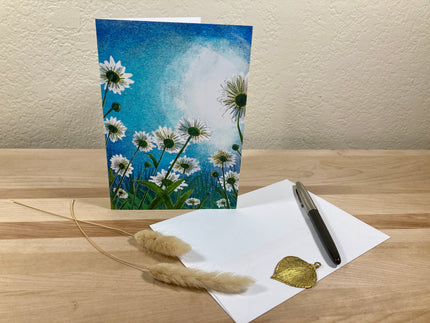 Greeting card with floral design, envelope, pen, and decorative elements on a wooden surface.