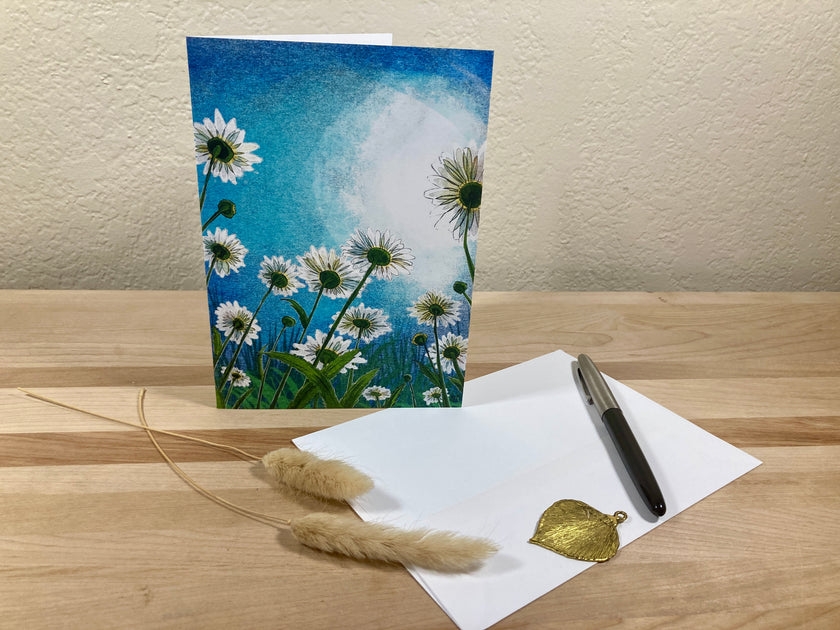 Greeting card with floral design, envelope, pen, and decorative elements on a wooden surface.